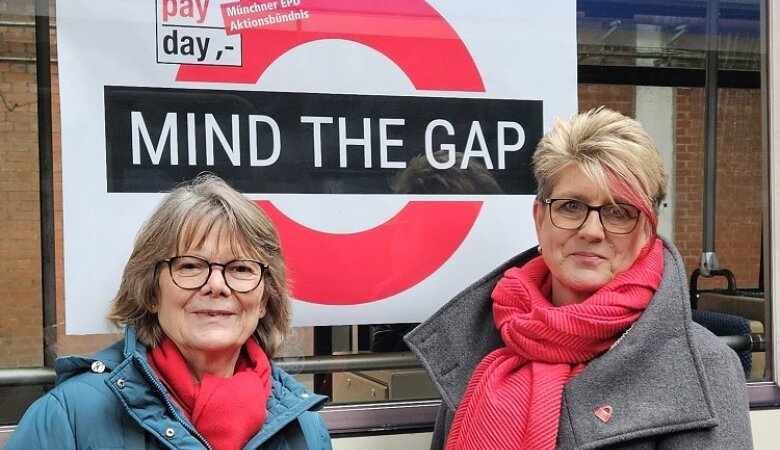 Katharina Geiger mit Christia Weigl-Schneider am Equal Pay Day 2024 vor einem Plakat mit der Aufschrift "Mind the Gap"